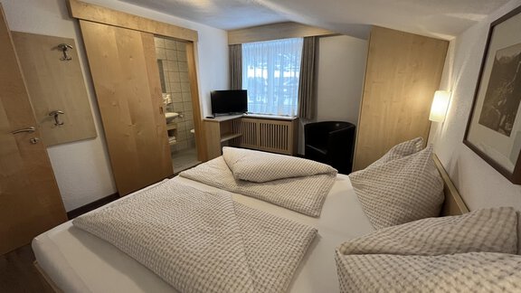 A cozy room with a double bed and modern wooden accents. There is a television and plenty of daylight coming through the window. - Franzele Appartements & Zimmer - Sölden