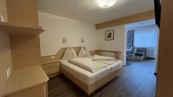 A simple bedroom with two single beds, nightstands, and a dresser. The room has a wooden floor and a window with natural light. - Franzele Appartements & Zimmer - Sölden