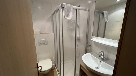 A modern bathroom with a shower, a sink, and a toilet. The walls are tiled in light colors and the room is well-lit. - Franzele Appartements & Zimmer - Sölden