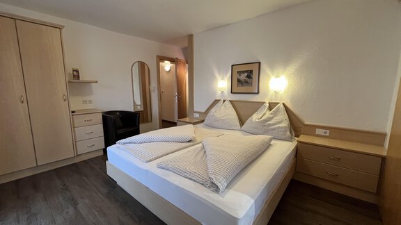 A simple bedroom with a double bed and wooden wardrobes. The walls are bright and the room feels cozy and inviting. - Franzele Appartements & Zimmer - Sölden