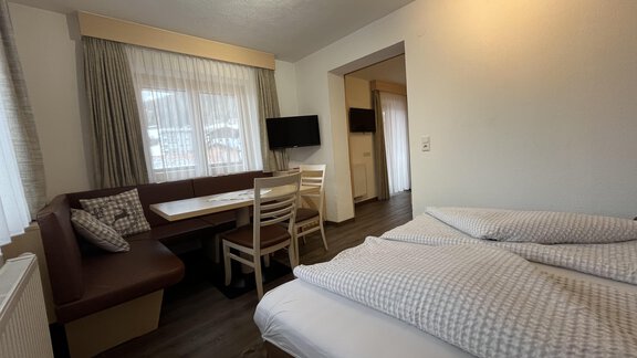A cozy room with a double bed, a table, and chairs. Bright curtains let in plenty of light. - Franzele Appartements & Zimmer - Sölden