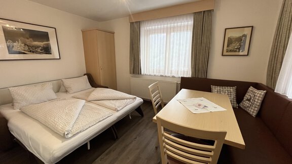 A cozy room with a double bed and a table with chairs. Bright windows create a friendly atmosphere. - Franzele Appartements & Zimmer - Sölden