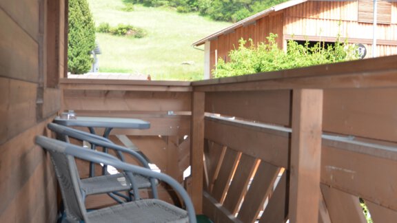 A cozy balcony with two chairs and a colorful flooring. In the background, green forests and a cabin can be seen. - Garni Columbia - Sölden