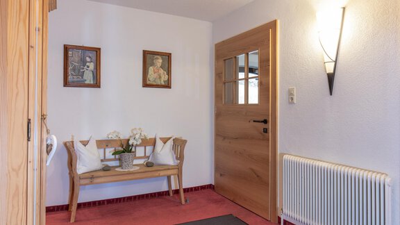 An inviting hallway with a wooden chair and two pictures on the wall. The walls are bright and the light creates a cozy atmosphere. - Garni Jaqueline - Sölden