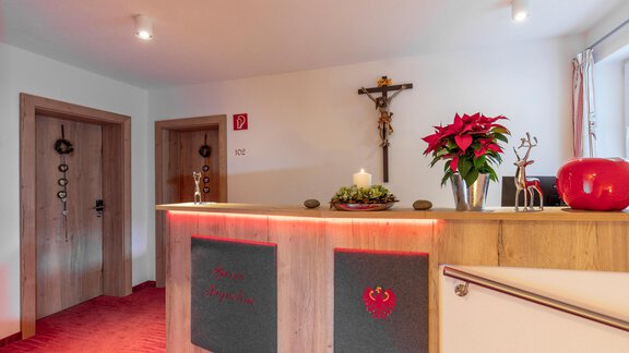 A reception desk in a cozy room with red accents. There are flowers and decorative elements on the table. - Garni Jaqueline - Sölden