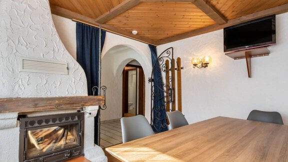 A cozy room with a wooden table, chairs, and a fireplace. The walls are light and the ceiling is clad with wood. - Garni Nadine - Sölden
