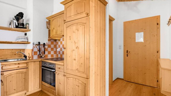 A cozy kitchen made of light wood with modern appliances. On the right, there is a wooden door that leads to the apartment. - Garni Nadine - Sölden
