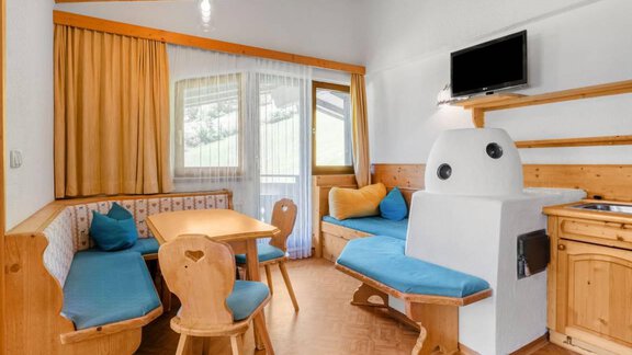 A cozy living area with wood paneling and blue cushions. A table and chairs provide space to relax, while a television is mounted on the wall. - Garni Nadine - Sölden