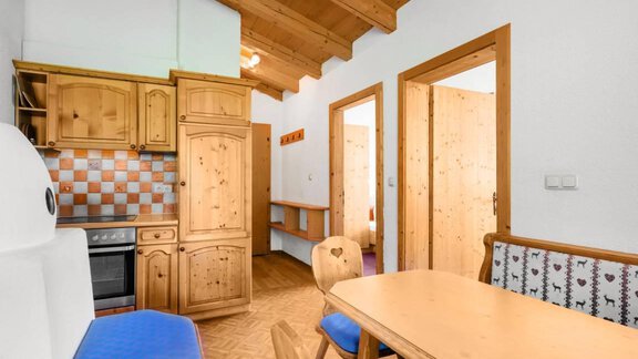 A cozy kitchen with wooden cabinets and a dining table. The walls are painted light and the floor is made of wood. - Garni Nadine - Sölden