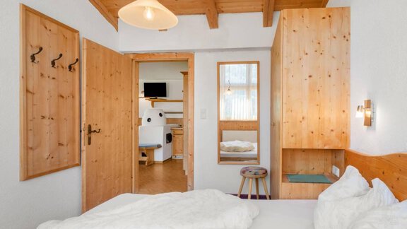 A cozy bedroom with wooden furniture and a view of an adjacent room. The walls are light, and the bed is furnished with white covers. - Garni Nadine - Sölden