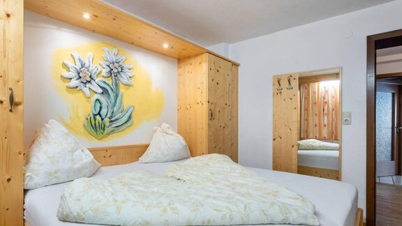 A cozy bedroom with a large bed and wooden paneling.  
On the wall hangs a painting of flowers that enlivens the room. - Garni Nadine - Sölden