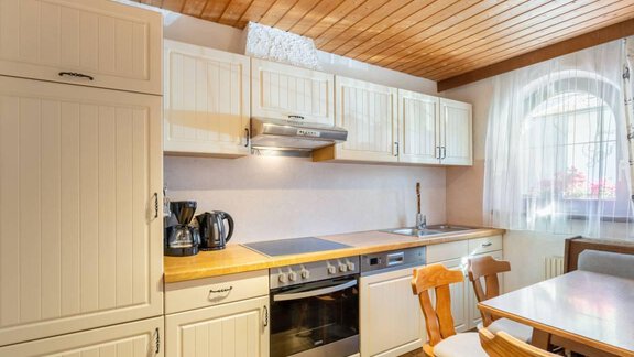 A modern kitchen with bright cabinets and wooden ceilings. The table is set with chairs and there is a stove and a coffee machine. - Garni Nadine - Sölden