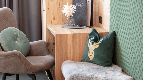 A cozy living area with a beige armchair and a green cushion. The wooden chest of drawers and the decorative elements give the room an inviting atmosphere. - Garni Rustica - Sölden