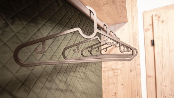 An elegant metal coat hanger is hanging on a wall. The background features a green, quilted surface and a wooden door. - Garni Rustica - Sölden