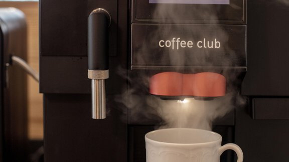 A coffee machine prepares a cup of coffee. Steam rises from the cup. - Garni Rustica - Sölden