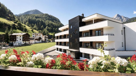 A modern building with balconies overlooks a picturesque landscape. In the foreground, colorful flowers are blooming, while the mountains are visible in the background. - Garni Rustica - Sölden