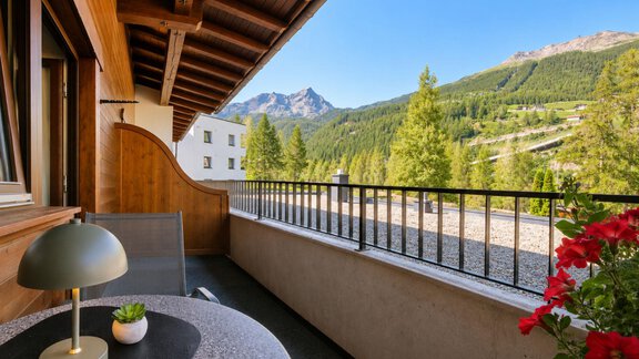 A cozy balcony with a view of the mountains and green trees. The table is decorated with a lamp and a small plant. - Garni Rustica - Sölden