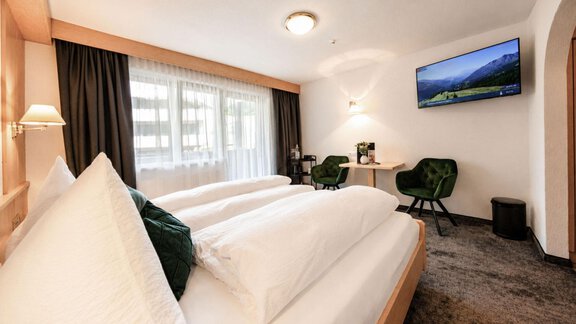 A modern hotel room with two single beds, a television, and a small table. A lot of natural light comes into the room through the windows. - Garni Rustica - Sölden