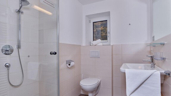A modern bathroom with a shower, a sink, and a toilet. The walls are light, and the design is simple and clean. - Gästehaus Bergkristall - Sölden