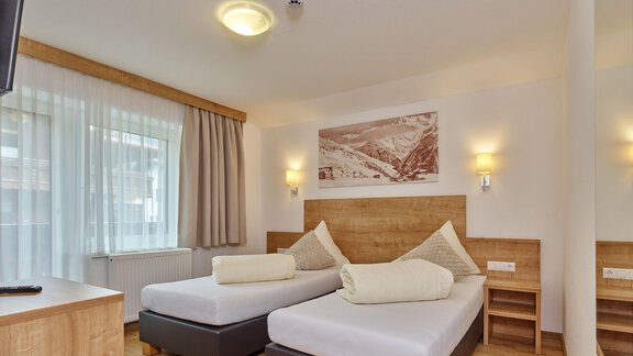 A cozy hotel room with two single beds and modern wooden interior. Large windows let in plenty of light and create a friendly atmosphere. - Gästehaus Bergkristall - Sölden