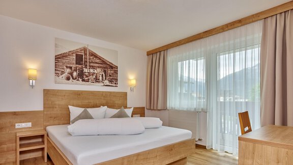 A modern bedroom with a large wooden bed and a friendly atmosphere.  
Large windows let in plenty of light and offer a view of nature. - Gästehaus Bergkristall - Sölden