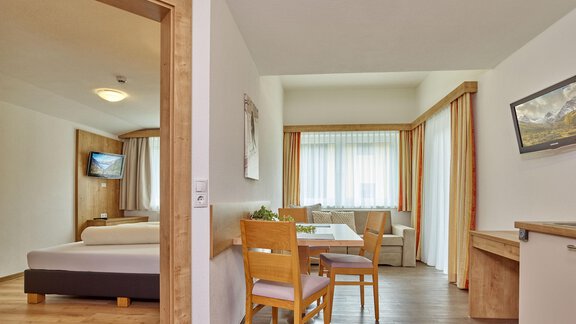 A bright and modern room with a cozy dining area and large windows. The space is furnished with wooden furniture and a television. - Gästehaus Bergkristall - Sölden