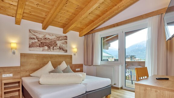 A modern bedroom with a wooden ceiling and large windows. There is a comfortable bed and a view of the mountains. - Gästehaus Bergkristall - Sölden