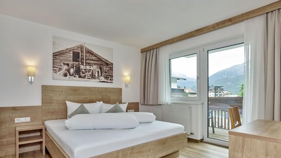 A modern room with wooden beds and a balcony. Large windows offer a view of the mountains and plenty of daylight. - Gästehaus Bergkristall - Sölden