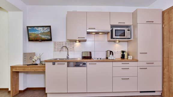 A modern kitchen with bright cabinets and a wooden countertop. In the background, a painting hangs on the wall. - Gästehaus Bergkristall - Sölden