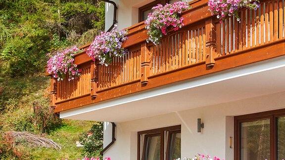 A charming wooden construction with balconies adorned with colorful flowers. In the background, a green, forested landscape is visible. - Gästehaus Bergkristall - Sölden