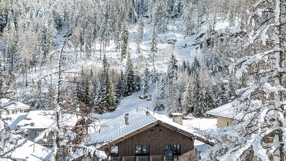 A picturesque winter village with snow-covered trees and mountains. In the foreground, a cozy wooden house can be seen. - Gästehaus Dr. Riml - Sölden