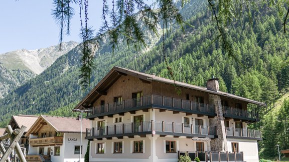 A beautiful hotel in the mountains, surrounded by green meadows and trees. In the foreground, playground equipment and bicycles can be seen. - Gästehaus Dr. Riml - Sölden