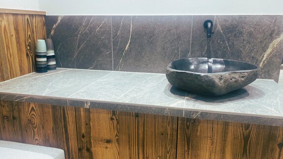 A modern bathroom view with an elegant black bowl on a gray table. In the background, wooden paneling and a faucet can be seen. - Gästehaus Europa - Sölden
