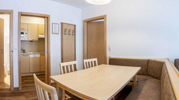 A bright dining area with a large table and a cozy seating corner. In the background, the kitchen is visible. - Gästehaus Europa - Sölden