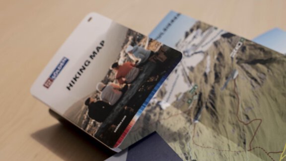 A stack of cards and business cards on a table. Below them, a hiking map and a business card from Thomas Pirpaner can be seen. - Gästehaus Europa - Sölden