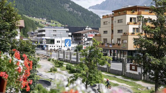 A picturesque view of a mountain road with a small village in the background. Flowers adorn the foreground, while the mountains surround the landscape. - Gästehaus Europa - Sölden