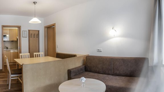 A bright living room with a couch and a round table. In the background, an open kitchen is visible. - Gästehaus Europa - Sölden