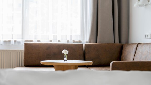 A cozy room with a brown sofa and a small table. On the table stands a vase with a flower. - Gästehaus Europa - Sölden