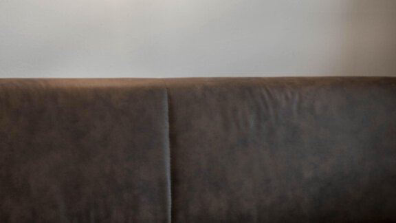 A cozy sofa with a warm wall lamp in the background. On a round table lie some brochures. - Gästehaus Europa - Sölden