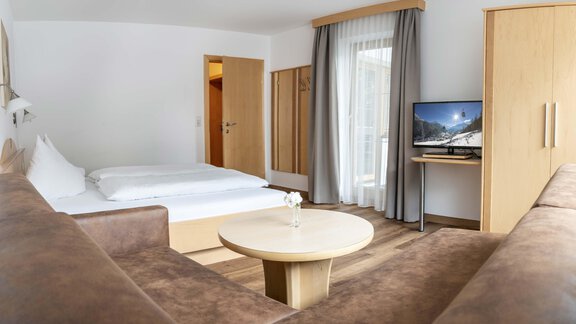 A spacious hotel room with a double bed and a seating area. A television and a table complete the modern furnishings. - Gästehaus Europa - Sölden