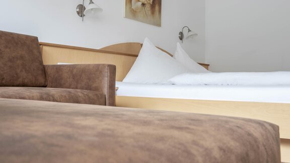 A cozy room with a brown sofa and a large bed. On the wall hangs a picture that decorates the room. - Gästehaus Europa - Sölden