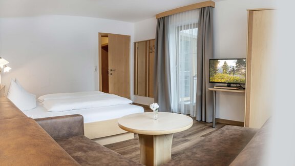 A modern room with a double bed, a cozy seating area, and a television. Large windows let in a lot of light and offer a view outside. - Gästehaus Europa - Sölden