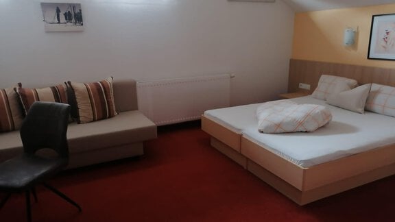 A cozy room with a double bed and a couch. The walls are light, and the floor is carpeted. - Gästehaus Sternberger - Sölden