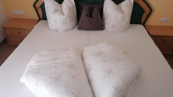 A bed with a white duvet and decorative pillows. The pillows are arranged in a heart shape, giving the room a cozy atmosphere. - Gästehaus Sternberger - Sölden