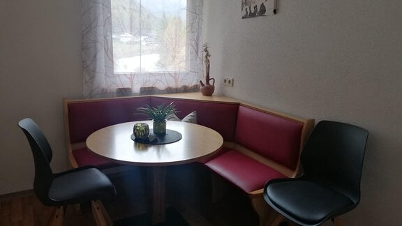 A cozy dining area with a round table and red benches. Next to the window is a decorative plant. - Gästehaus Sternberger - Sölden