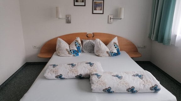 A cozy bedroom with a large bed and decorative pillows. The walls are light, and there are curtains in gentle colors. - Gästehaus Sternberger - Sölden
