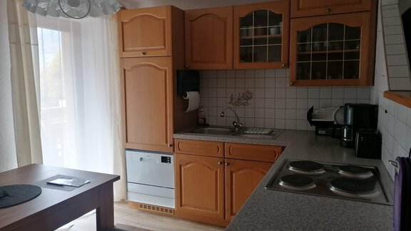 A bright kitchen with wooden cabinets and a dining area. It is equipped with a refrigerator and modern cooktops. - Gästehaus Sternberger - Sölden
