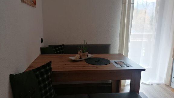 A cozy dining area with a wooden table and a bench. The light streams through the window, creating an inviting atmosphere. - Gästehaus Sternberger - Sölden