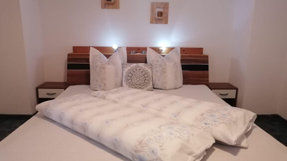 A modern bedroom with a large bed and decorative pillows. The walls are light, and there are stylish nightstands as well as subtle lighting. - Gästehaus Sternberger - Sölden