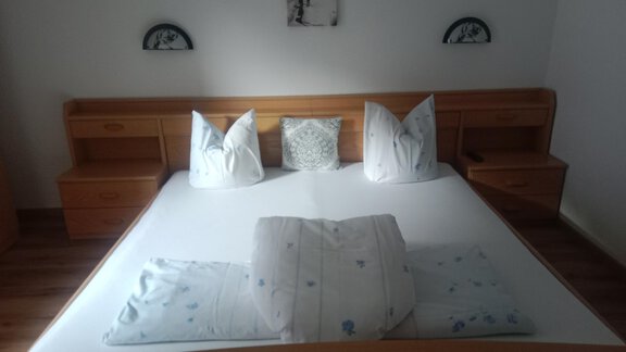 A cozy bedroom with a large bed and white pillows. The walls are light, and wooden drawers provide storage space. - Gästehaus Sternberger - Sölden